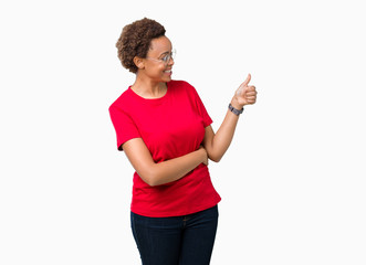 Beautiful young african american woman wearing glasses over isolated background Looking proud, smiling doing thumbs up gesture to the side