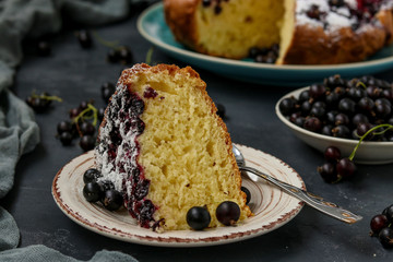 Homemade cottage pie with black currant with a cut piece of cake located on a dark background, horizontal orientation