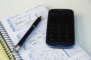 Naklejka na ściany i meble Smartphone, pen, hand, note book or phone book or organizer with some notes, info or phones number on a white table. Plans and agenda. Keyboard on.