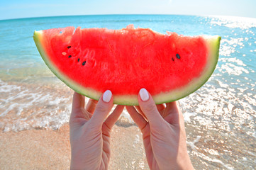 Summertime concept with watermelon slice in woman hand against the sea