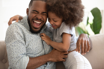 Excited african american dad tickling little daughter.