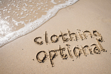 Clothing optional nudist message handwritten in simple text on smooth sand beach with incoming wave