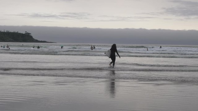 Wide, slow motion, surfer with a board walking into the sea, Vancouver Island