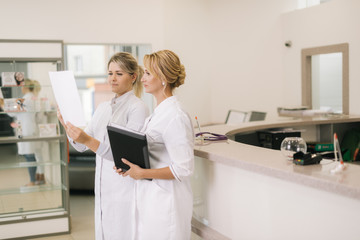 Obraz premium Two woman doctors are looking at the results of the medical tests. Two doctors standing by counter and looking at document in the hospital