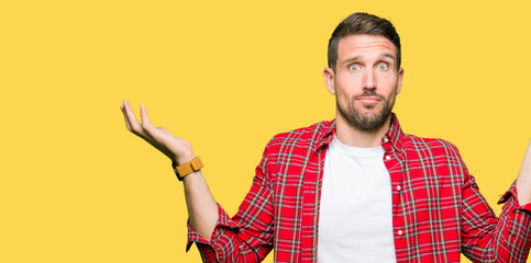 Handsome man wearing casual shirt clueless and confused expression with arms and hands raised....
