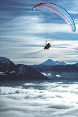 paraglider above clouds with snowy mountains in background
