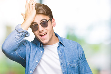 Young handsome man wearing sunglasses over isolated background surprised with hand on head for mistake, remember error. Forgot, bad memory concept.