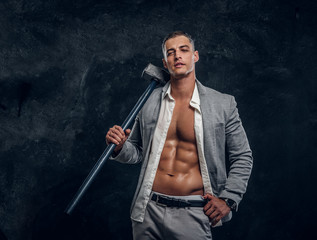Young attractive hot man in suit and opened white shirt is holding long hammer in hand.