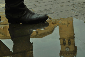 Bota de hombre antigua reflajada en un charco de agua después de haber llovido. Iglesia española...