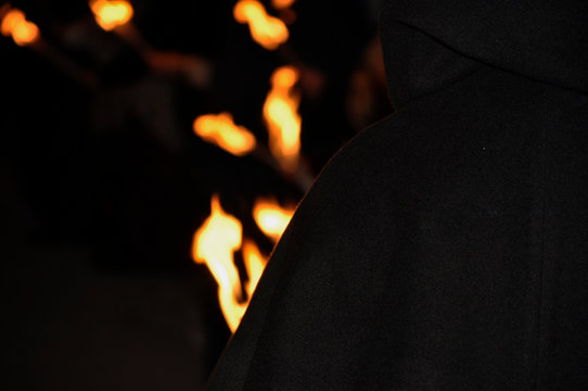 Hombre o mago encapuchado de espaldas y antorchas de fuego brillando radiantes en el fondo 