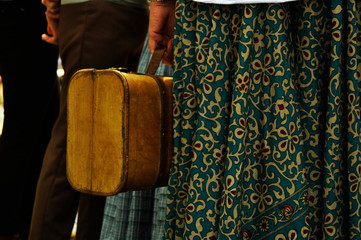 Extremidades. Señora sosteniendo una maleta antigua, rodeada de gente esperando el tren. Maleta o...