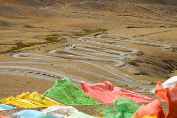 CLOSE UP: Colorful prayer flags flutter above serpentine road across Gawula Pass