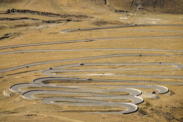 Locals and tourists slowly drive along the asphalt road winding a barren hill.