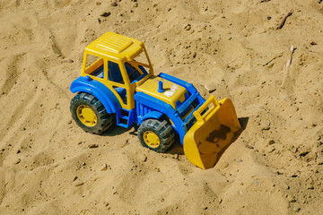 blue and yellow tractor on the sand. Baby's toys outdoor