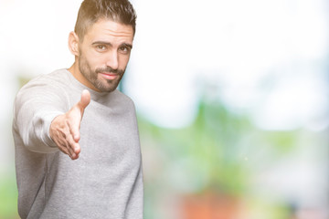 Young handsome man wearing sweatshirt over isolated background smiling friendly offering handshake as greeting and welcoming. Successful business.