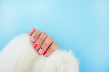 Young woman's hand with beautiful manicure on blue color background holding piece of white faux fur.