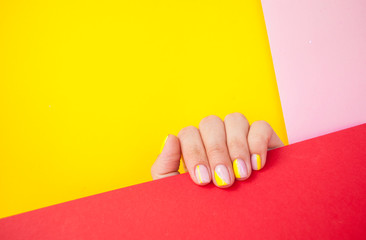 Young woman's hand with beautiful manicure on yellow and pink background holding red color paper with copyspace.