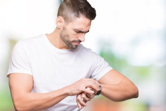 Handsome man wearing white t-shirt over outdoors background Checking the time on wrist watch, relaxed and confident