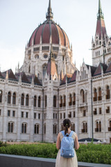 budapest travel: brunette tourist girl with a backpack in a dress stands near the Hungarian Parliament 1