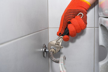 Plumber installs of a toilet hose in a hard-to-reach place with an adjustable wrench.