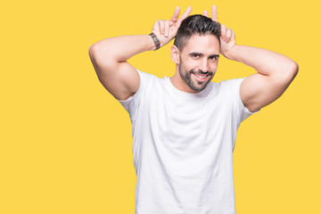 Fototapeta na wymiar Handsome man wearing white t-shirt over yellow isolated background Posing funny and crazy with fingers on head as bunny ears, smiling cheerful