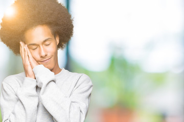 Young african american man with afro hair wearing sporty sweatshirt sleeping tired dreaming and posing with hands together while smiling with closed eyes.