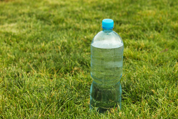 Plastic bottle with mineral water stands on a green grass in the park, horizontal orientation, copy space