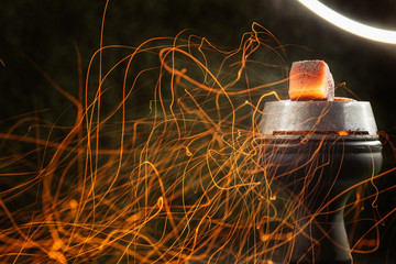  red-hot coals lie on a bowl of a hookah and sparks fly from them in different directions. on a...