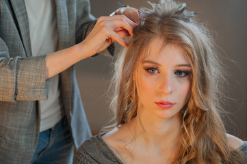 Makeup artist and hairdresser are preparing bride before wedding. Hairdresser-stylist with short stylish hairstyle applies makeup, makes false eyelashes, paints lips, curls girl, spectacular lighting