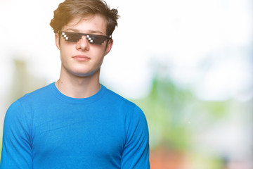 Young man wearing funny thug life glasses over isolated background with serious expression on face. Simple and natural looking at the camera.