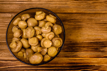 Glass bowl with canned mushrooms on wooden table. Top view