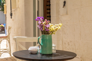 Italy, Apulia, Metropolitan City of Bari, Monopoli. Vase of flowers on a cafe table.