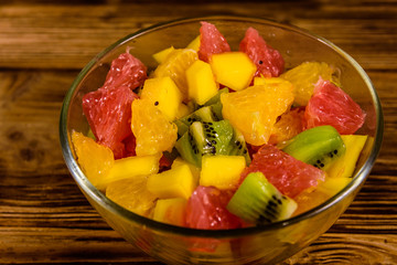 Salad with mango, oranges, grapefruit and kiwi fruits in a glass bowl on wooden table