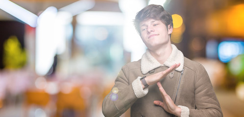Young handsome man wearing winter coat over isolated background Doing time out gesture with hands,...