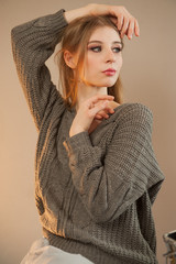 young blonde in gray sweater with open shoulders. woman poses for the camera, demonstrating natural beauty with beautiful make-up and curled hair. Tender emotions and coquetry