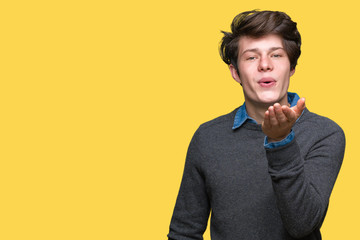 Young handsome elegant man over isolated background looking at the camera blowing a kiss with hand on air being lovely and sexy. Love expression.