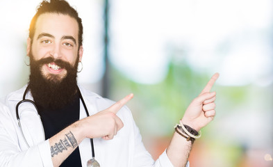 Naklejka premium Doctor with long hair wearing medical coat and stethoscope smiling and looking at the camera pointing with two hands and fingers to the side.