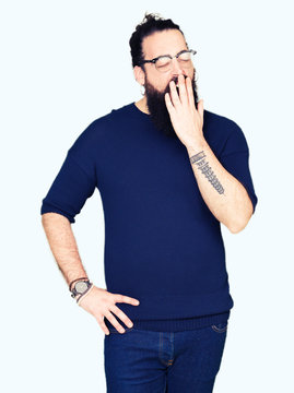 Young hipster man with long hair and beard wearing glasses bored yawning tired covering mouth with hand. Restless and sleepiness.