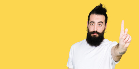 Young hipster man with long hair and beard wearing casual white t-shirt Pointing with finger up and angry expression