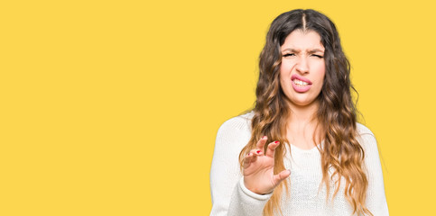 Young beautiful woman wearing white sweater disgusted expression, displeased and fearful doing...
