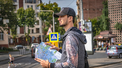 Young happy tourist sightseeing in city. Cheerful man wanderer with trendy look searching direction...