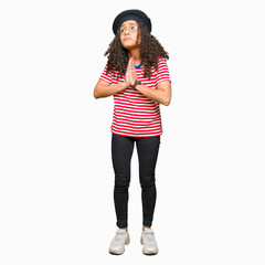 Young beautiful woman with curly hair wearing glasses and fashion beret begging and praying with hands together with hope expression on face very emotional and worried. Asking for forgiveness. 