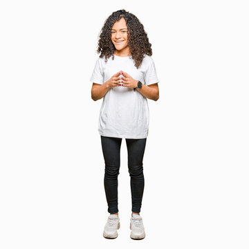 Young beautiful woman with curly hair wearing white t-shirt Hands together and fingers crossed smiling relaxed and cheerful. Success and optimistic