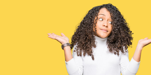 Young beautiful woman with curly hair wearing turtleneck sweater clueless and confused expression...