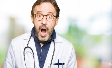 Handsome middle age doctor man wearing medical coat afraid and shocked with surprise expression, fear and excited face.