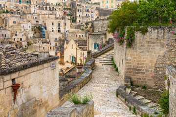 Italy, Basilicata, Province of Matera, Matera. View of buildings and stone wall along a cobblestone walkway.