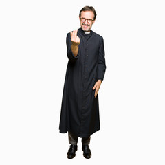 Middle age priest man wearing catholic robe Beckoning come here gesture with hand inviting happy and smiling