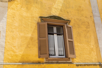 Italy, Basilicata, Province of Matera, Matera. Window with lace curtains and shutters in a yellow wall.
