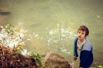 Curly haired white boy on the banks of a river in the forest looks up. Space for text