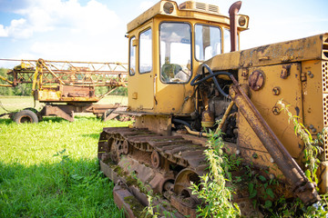 Fototapeta na wymiar Abandoned farm equipment. The bulldozer covered with moss. Overgrown weeds tractor. Bulldozer is worth many, many years.